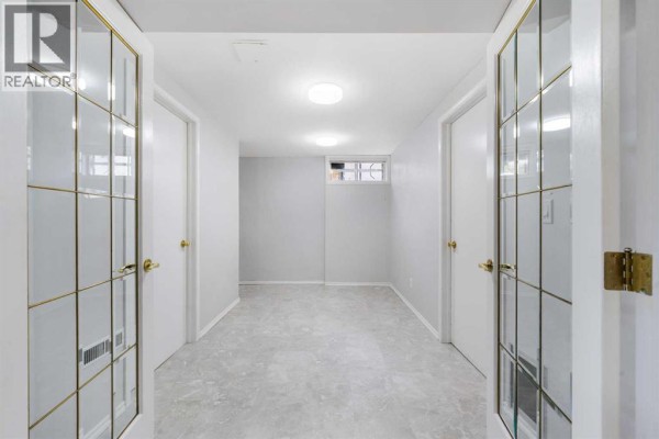 Hallway in the basement with grey tile flooring, white doors, and glass-paneled double doors. - 479 Bracewood Crescent Sw, Calgary