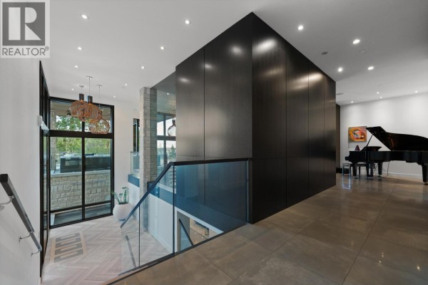 Interior view of staircase with glass railing, dark wood paneling, and piano - 4799 Clovelly Walk, West Vancouver