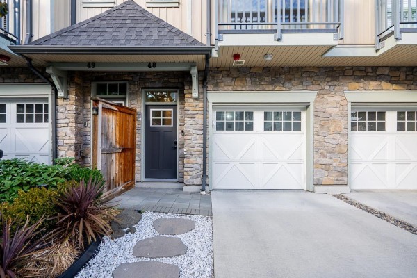 Close-up of townhouse entrance with dark grey door, wooden gate, stone facade, and white garage doors. - 48 20487 65 Avenue, Langley