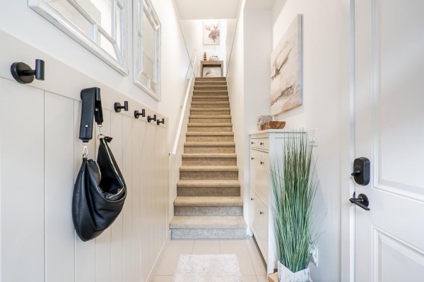 Interior entryway with white paneled walls, coat hooks, stairs, shoe cabinet, and artwork. - 48 20487 65 Avenue, Langley
