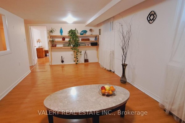 Living area with hardwood floors, oval coffee table, and shelving unit with decor. - 48 Dunkirk Road, Toronto