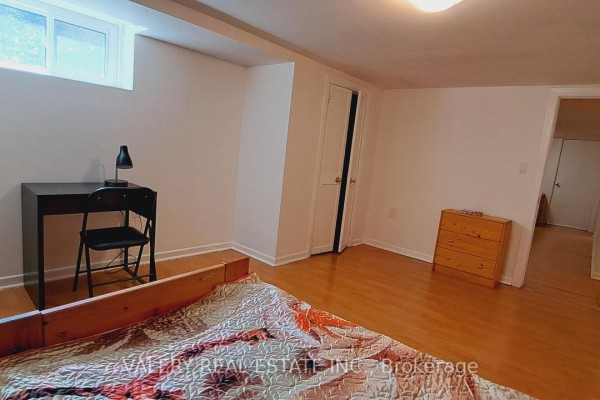 Bedroom with a wooden bed frame, desk with chair, and a dresser by the door. - 48 Dunkirk Road, Toronto