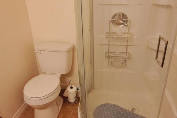 Bathroom with a toilet, toilet paper holder, and a corner shower stall with glass doors. - 48 Dunkirk Road, Toronto