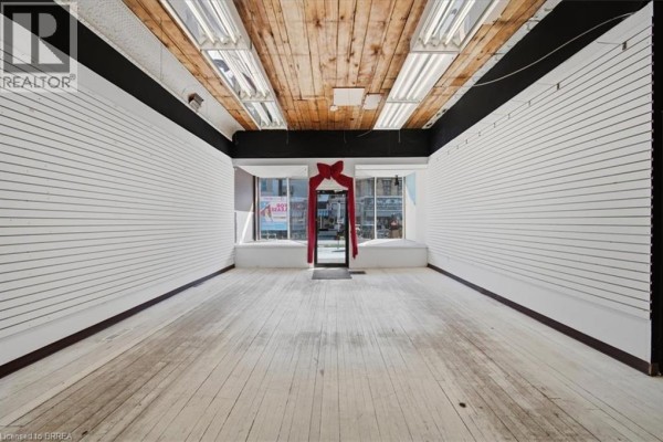 Empty interior commercial space with white slat walls, wooden ceiling, and wood floors facing front windows. - 48 Grand River Street N, Paris