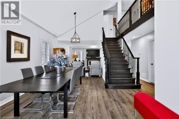 Dining area with a dark wood table and grey chairs, adjacent to a living room and dark wood staircase. - 48 Holkham Avenue, Ancaster