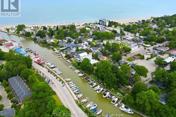 Aerial view of a canal with docked boats, townhouses, and beach in the distance. - 48 Lake Road, Lambton Shores