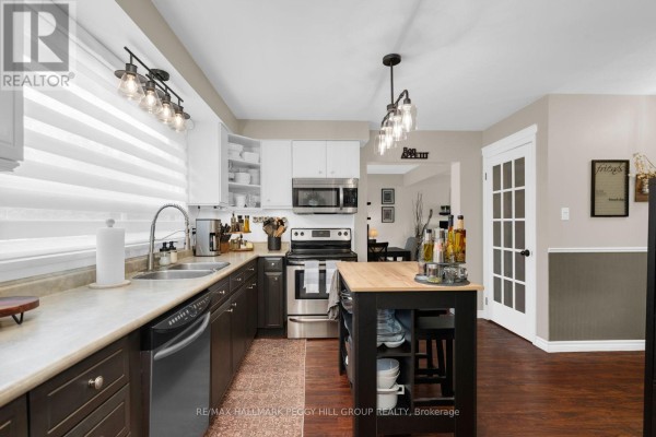 Kitchen with dark wood lower cabinets, white upper cabinets, stainless steel appliances, and a butcher block island. - 48 Oren Boulevard, Barrie
