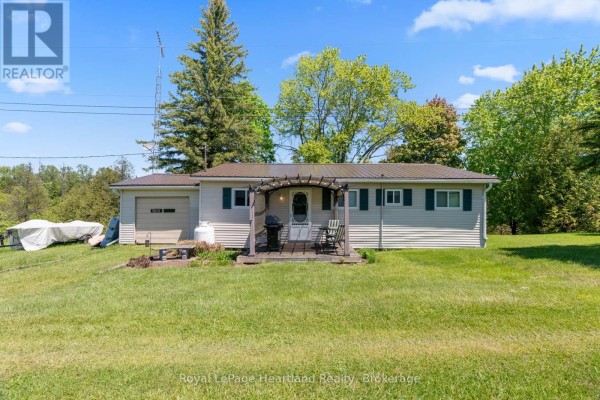 Front view of a light beige house with a brown metal roof, a detached garage, and a small front porch with a grill. - 48 Poechman Lane, Brockton