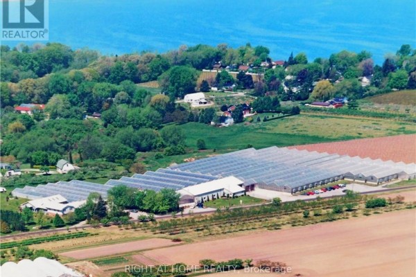 Aerial view of a commercial property with greenhouses and vineyards, showing a road and surrounding green landscape. - 48 Roven Road, Niagara On The Lake