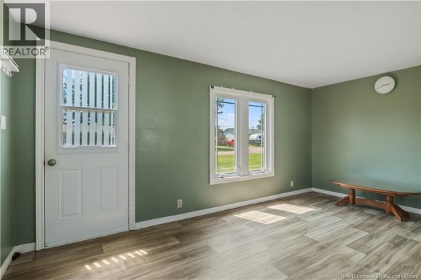Living room with pale green walls, a white door, a window, light wood laminate flooring, and a small wooden bench. - 48 Rue Des Copains, Richibucto