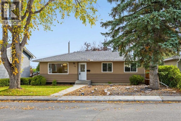 Front exterior of a bungalow with a tan and brown stucco finish and a white front door. - 48 Selkirk Drive Sw, Calgary