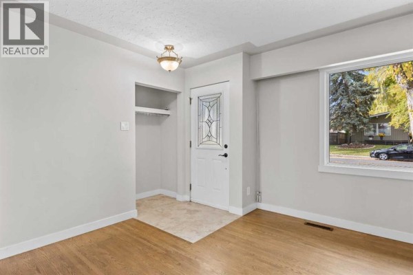 Entranceway with a white door, tiled floor, wood floor, and a small closet with shelving. - 48 Selkirk Drive Sw, Calgary