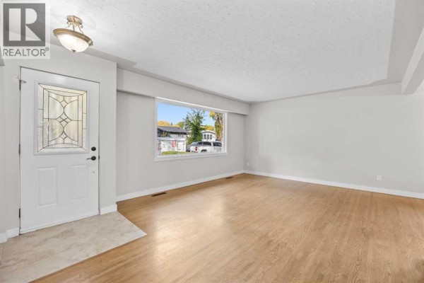 Living room with light gray walls, hardwood floors, and a large window overlooking the street. - 48 Selkirk Drive Sw, Calgary