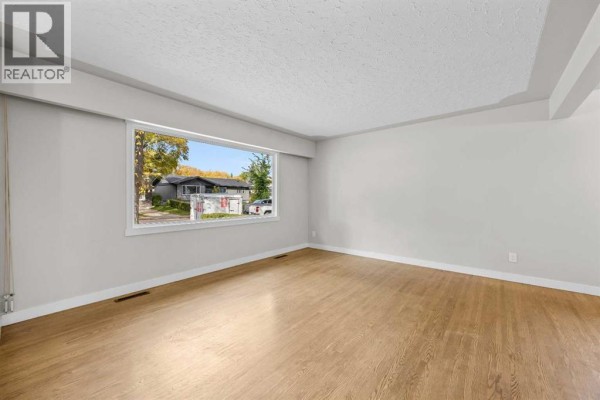 Spacious living room with light gray walls, hardwood floors, and a large window with a view of houses. - 48 Selkirk Drive Sw, Calgary