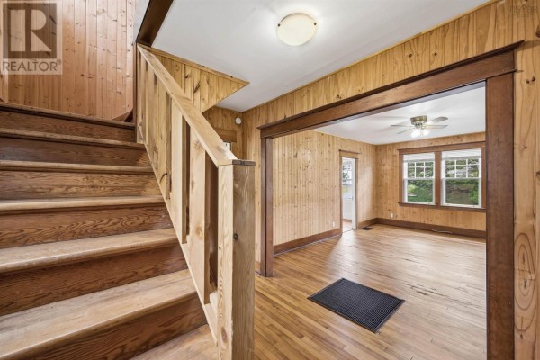 Wooden staircase leading upstairs, adjacent to a living room with wood-paneled walls and hardwood floors. - 48 Shankel Road, Hubbards