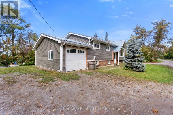 Side view of a grey house with a white garage door, brick foundation, and dark siding. - 48 Sliverbirch Street, Kawartha Lakes