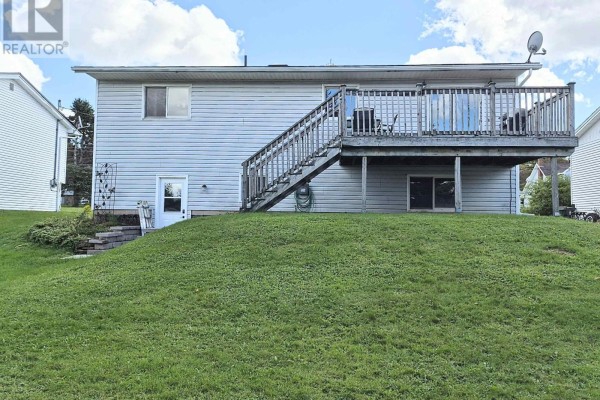 View of the backyard with a deck and a sloped lawn leading to a patio area with stone steps. - 48 Townshend Avenue, Amherst