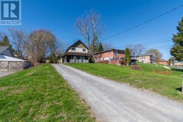 Gravel driveway leading up to a house on a grassy slope with surrounding trees. - 48 Wallbridge Crescent, Belleville
