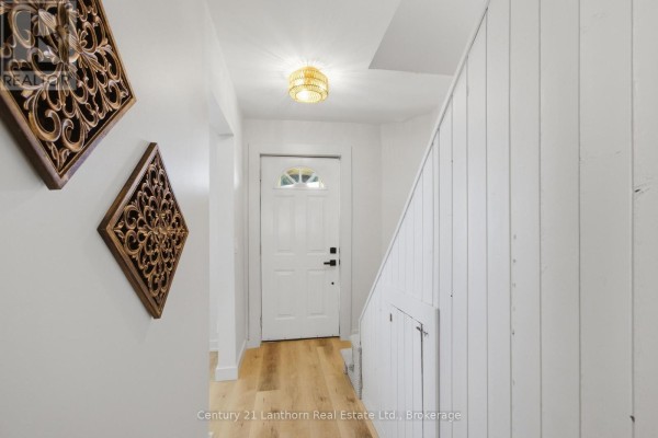 Interior hallway with a white door, wood-look floor, and decorative wall art. - 48 Wallbridge Crescent, Belleville