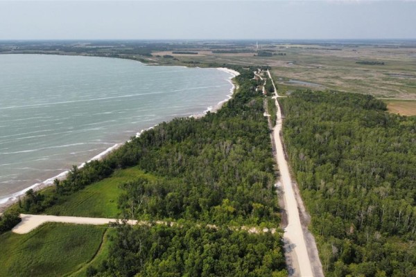 Aerial view of a lake's shoreline with trees, a dirt road, and fields in the distance. - 48 Watchorn Landing Road, Moosehorn