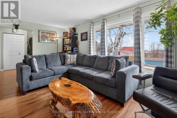 Living room with a sectional sofa, large wooden coffee table, and windows overlooking a treed landscape. - 480 Broderick Street, Tay