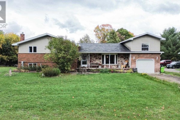 Front view of a house with stone and brick exterior, porch, large windows, and manicured lawn. - 480 Moss Rd, Sault Ste  Marie