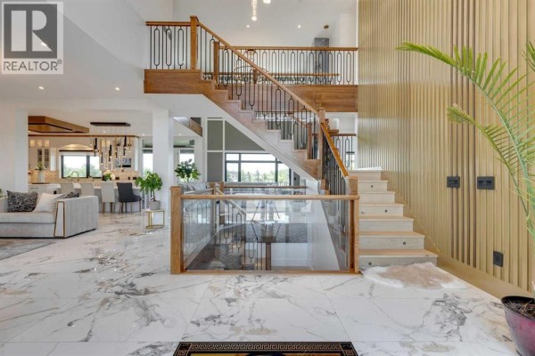 Grand entryway with marble floors, a wood staircase with metal railings, and glass railings. - 48017 Harvest Lane E, Rural Foothills County