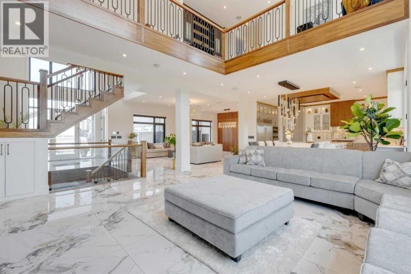 Spacious open-concept living area with grey sectional sofa, ottoman, and view of kitchen. - 48017 Harvest Lane E, Rural Foothills County