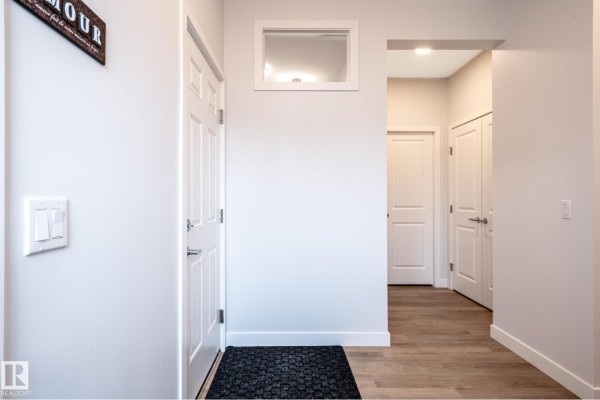 View from entryway looking down a hallway with white doors and light wood floors. - 4804 Cawsey Tc Sw, Edmonton