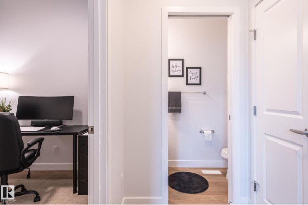 View of a home office desk and a small bathroom with framed art above the toilet. - 4804 Cawsey Tc Sw, Edmonton