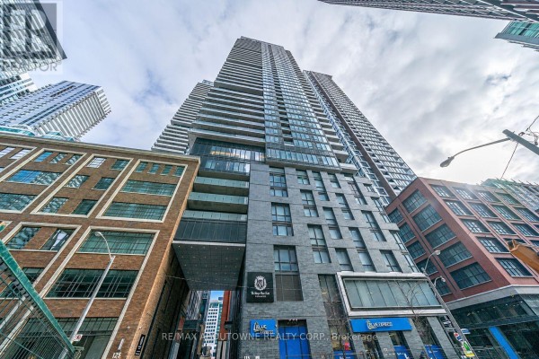 Low-angle view looking up at a tall, modern apartment building with balconies and glass facade. - 4805 - 115 Blue Jays Way, Toronto