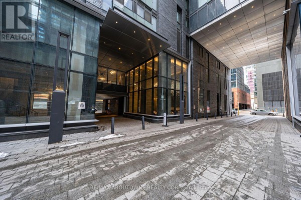 Exterior view of a modern apartment building entrance with a covered driveway and cobblestone walkway. - 4805 - 115 Blue Jays Way, Toronto