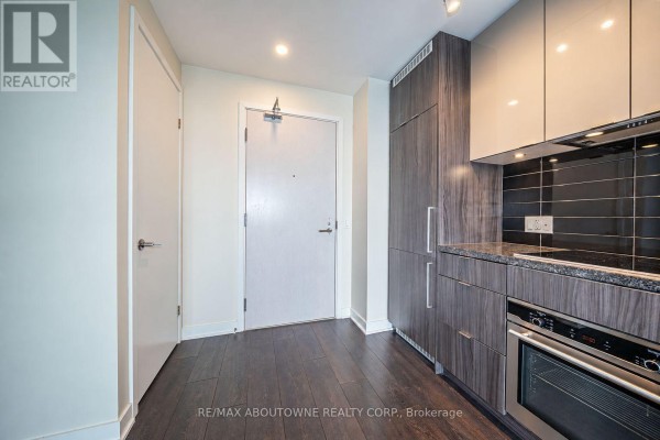 Apartment entryway with a white door, closet, and a modern kitchen with dark wood cabinetry. - 4805 - 115 Blue Jays Way, Toronto