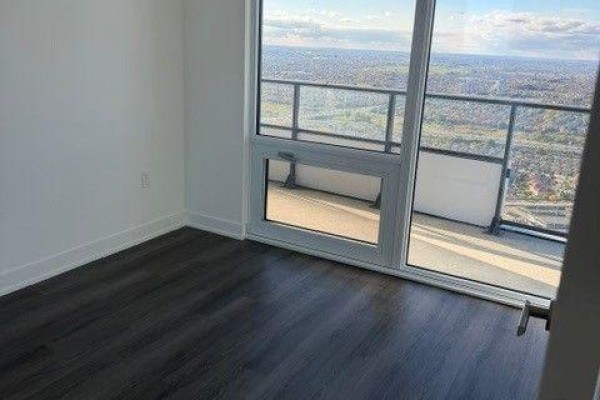 Bedroom with dark wood floors, white walls, and access to a balcony. - 4805 - 448 Burnhamthorpe Road W, Mississauga