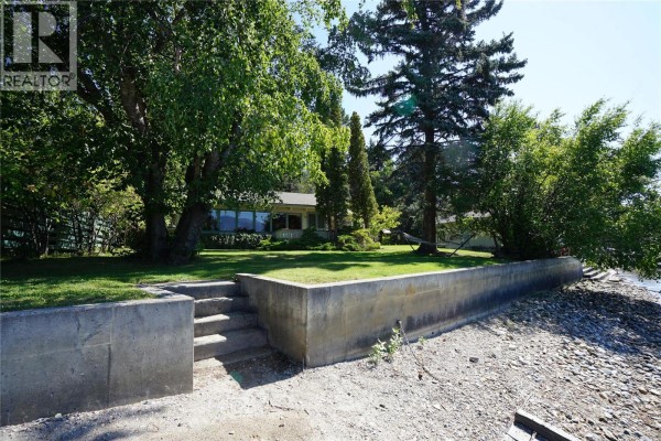 Concrete retaining wall with stairs leading to a rocky shoreline and a house. - 4806 Andreen Road, Windermere