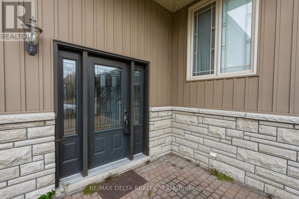 Close-up of the front entrance of a beige house, featuring a dark grey door with glass panels and stone accents. - 4806 Frank Kenny Road, Ottawa