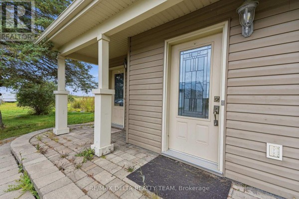 A covered walkway with white pillars leads to a beige front door with decorative glass panels on the side of the house. - 4806 Frank Kenny Road, Ottawa
