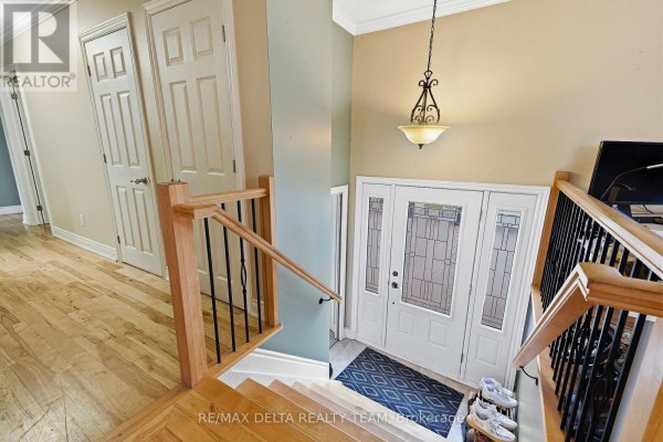 View from above of a bright foyer with double white doors, a wooden staircase with black spindles, and light wood floors. - 4806 Frank Kenny Road, Ottawa