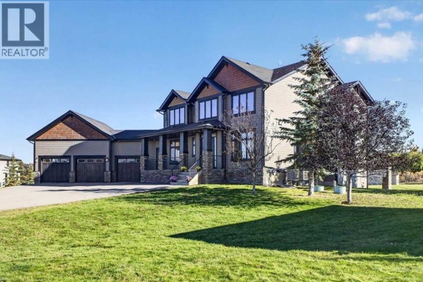 Side view of a large home with grey siding, dark trim, and attached garage. - 48061 279 Avenue E, Rural Foothills County
