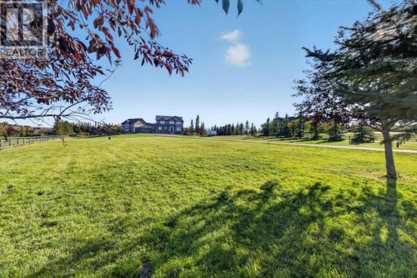 Expansive green lawn with mature trees and a distant view of the house. - 48061 279 Avenue E, Rural Foothills County