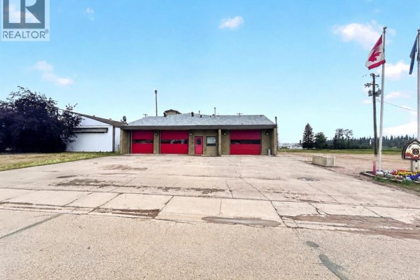 Wide exterior shot of a fire hall with red bay doors and a concrete lot. - 4808 50 Street, Fort Vermilion