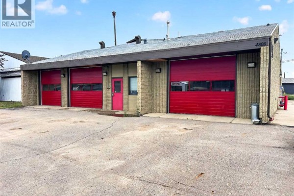 Close-up of the building exterior showing three red bay doors, tan siding, and signage. - 4808 50 Street, Fort Vermilion