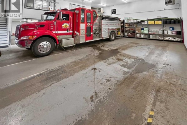 Interior view of a fire hall with a red fire truck, storage shelves, and a concrete floor. - 4808 50 Street, Fort Vermilion