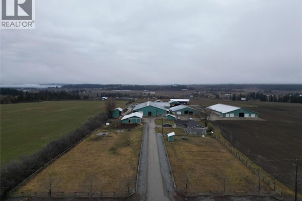 Exterior view of a single-story house with a garage, lawn, and farm buildings in the background. - 4809 Back Enderby Road, Spallumcheen