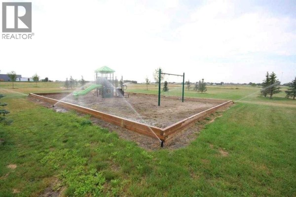 A playground surrounded by a wooden border with sprinklers watering the sandy ground and grass. - 4810 72 Ave., Taber
