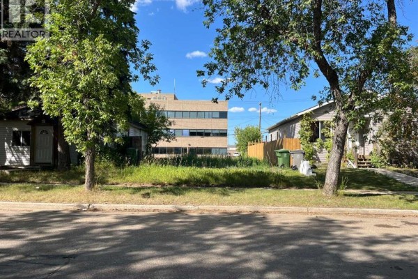 View of the lot from the street, featuring trees and nearby buildings in the background. - 4814 49 Street, Lloydminster