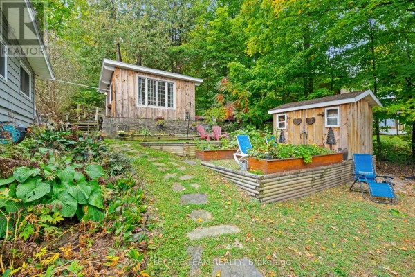 Backyard with two wooden sheds, raised garden beds, and stone path. - 4819 Opeongo Road, Ottawa