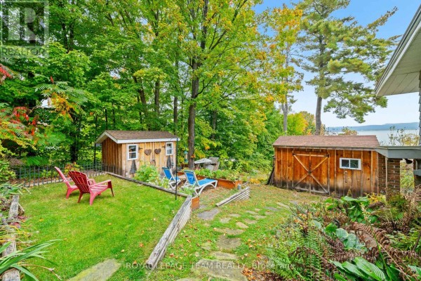 View of the backyard with garden beds, sheds, and a distant body of water. - 4819 Opeongo Road, Ottawa