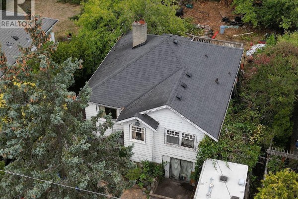 Aerial view of a white house with a dark shingle roof surrounded by trees and greenery. - 482 Ker Ave, Saanich
