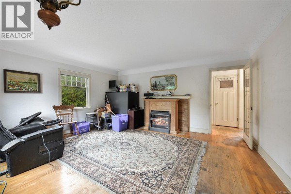 Living room with a patterned rug, fireplace, wooden floor, and doorway to another room. - 482 Ker Ave, Saanich